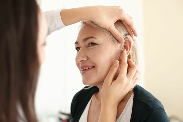 Un’otorinalaringoiatra sistema un apparecchio acustico nell’orecchio di una donna.