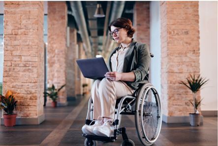Una donna in sedia a rotelle mentre usa un portatile poggiato sulle sue gambe.