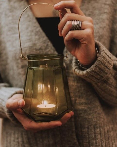 Particolare delle mani di una donna che reggono una lampada con al suo interno un lume acceso (fotografia di lil artsy su Pexels).