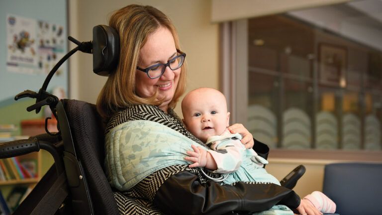 Una madre in sedia a rotelle sorride mentre tiene in braccio la sua neonata.