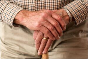 Particolare delle mani di un uomo anziano poggiate su un bastone (foto di Pexels).