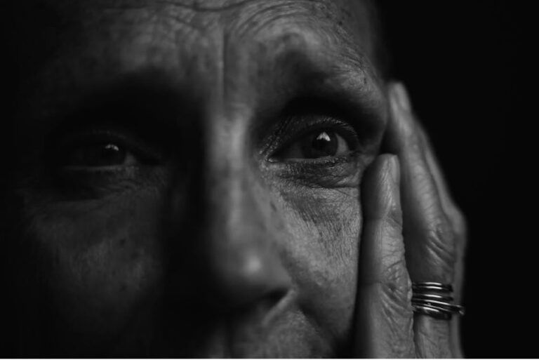 Uno scatto in bianco e nero ritrae parte del volto di una donna anziana che poggia una mano sulla tempia (foto di Matej su Pexels).