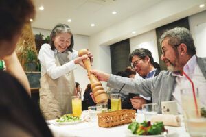Una cameriera con demenza in difficoltà con un grosso macinapepe viene aiutata dagli ospiti del “Ristorante degli ordini sbagliati” di Tokyo, in un’atmosfera cordiale e divertita.