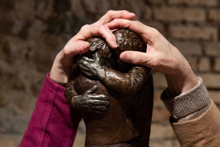 Particolare di due persone che esplorano con le mani una statua di bronzo di medie dimensioni raffigurante due persone abbracciate (fonte: Museo Tattile Statale Omero di Ancona).